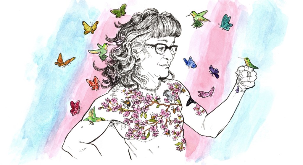 A muscular woman, missing their breasts and covered with tattoos of cherry blossoms populated with bees, butterflies, and a hummingbird, eyes the hummingbird perched on their finger like they’re friends. More hummingbirds, and a rainbow of butterflies, fly around them. The colors of the trans flag flow diagonally across the background.